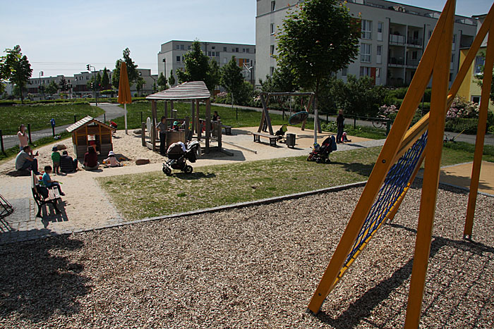 Blick vom Klettergerüst auf die Sandspielecke und Nestschaukel.